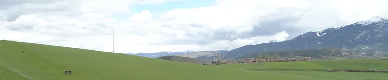 Paisatge de camps verds i muntanyes amb neu al fons